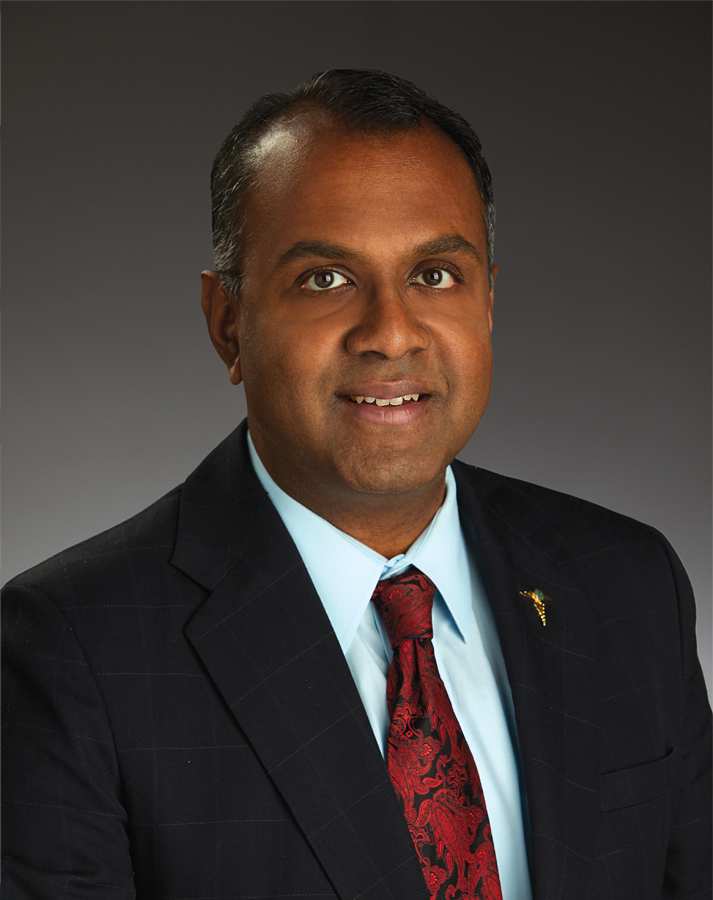 Dr. Bala Ambati, Ophthalmologist and Vision Researcher - Pacific Clear Vision Eugene Professional headshot of Dr. Bala Ambati, an accomplished ophthalmologist and vision science researcher, wearing a dark suit, light blue shirt, and red patterned tie, set against a neutral gray background. - Pacific Clear Vision Eugene