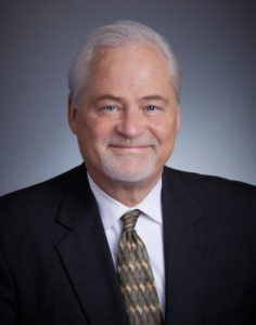Dr. Bradley Lorenzen - Pacific Clear Vision Eugene Professional headshot of Dr. Bradley Lorenzen wearing a dark suit, white shirt, and patterned tie, smiling against a neutral background. - Pacific Clear Vision Eugene